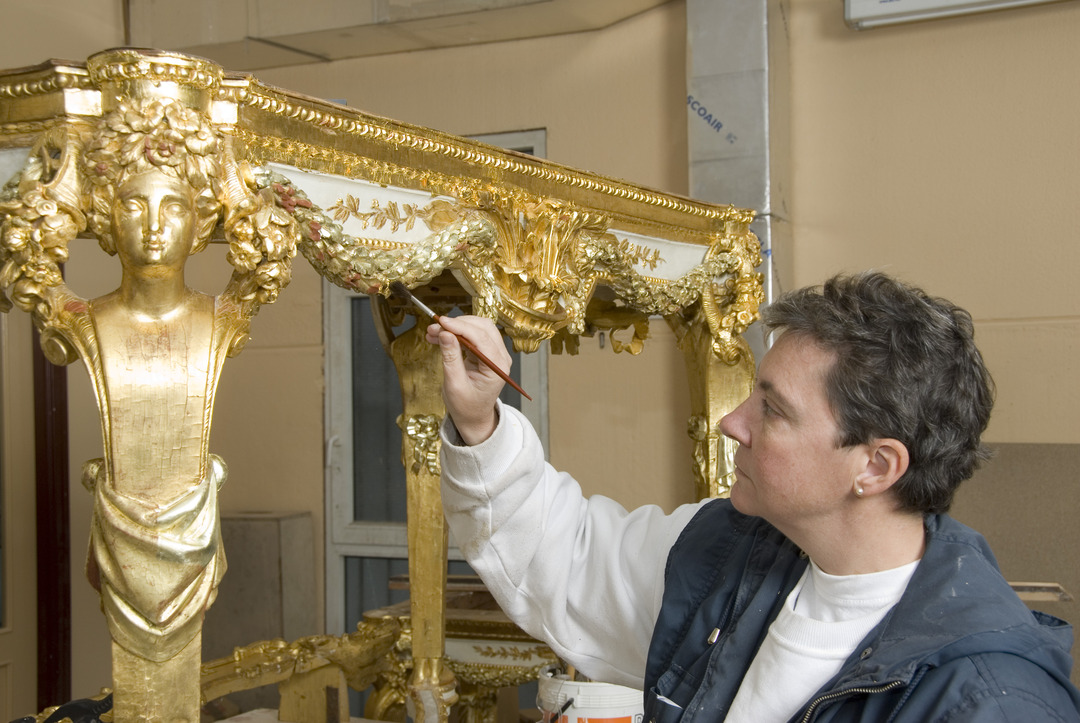 Conservadora aplicando oro fino a un moviliario artístico.